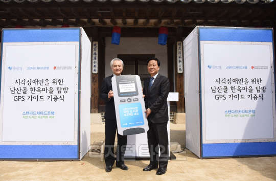 박종복 스탠다드차타드은행장(왼쪽)이 8일 서울시 중구 남산골 한옥마을에서 정효성 서울시 행정 1부시장에게 시각장애인을 위한 남산골 한옥마을 탐방 GPS(위성위치확인시스템) 가이드 20개를 전달하고 있다.